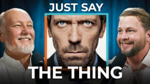 Two men speak into microphones on either side of an intense face. Bold text reads: "Just Say The Thing." Value clarity every time.