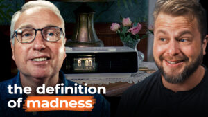 Two men smile in front of a vintage clock and flowers. Text reads "the definition of madness"—a quirky take on construction hiring.