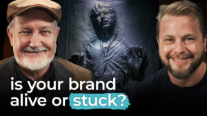 Two men smile with a frozen figure behind them. Text in front reads "is your brand alive or stuck?" highlighting brand consistency.